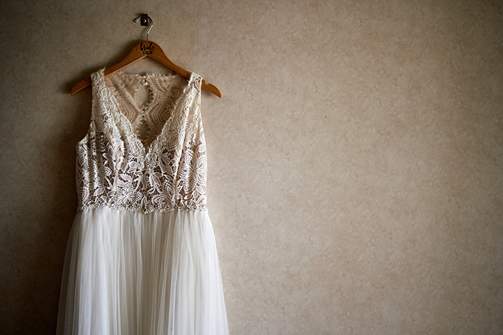 A wedding dress hanging on a hanger against a gray backdrop, prepared for UOVO Fashion’s wedding wardrobe storage.