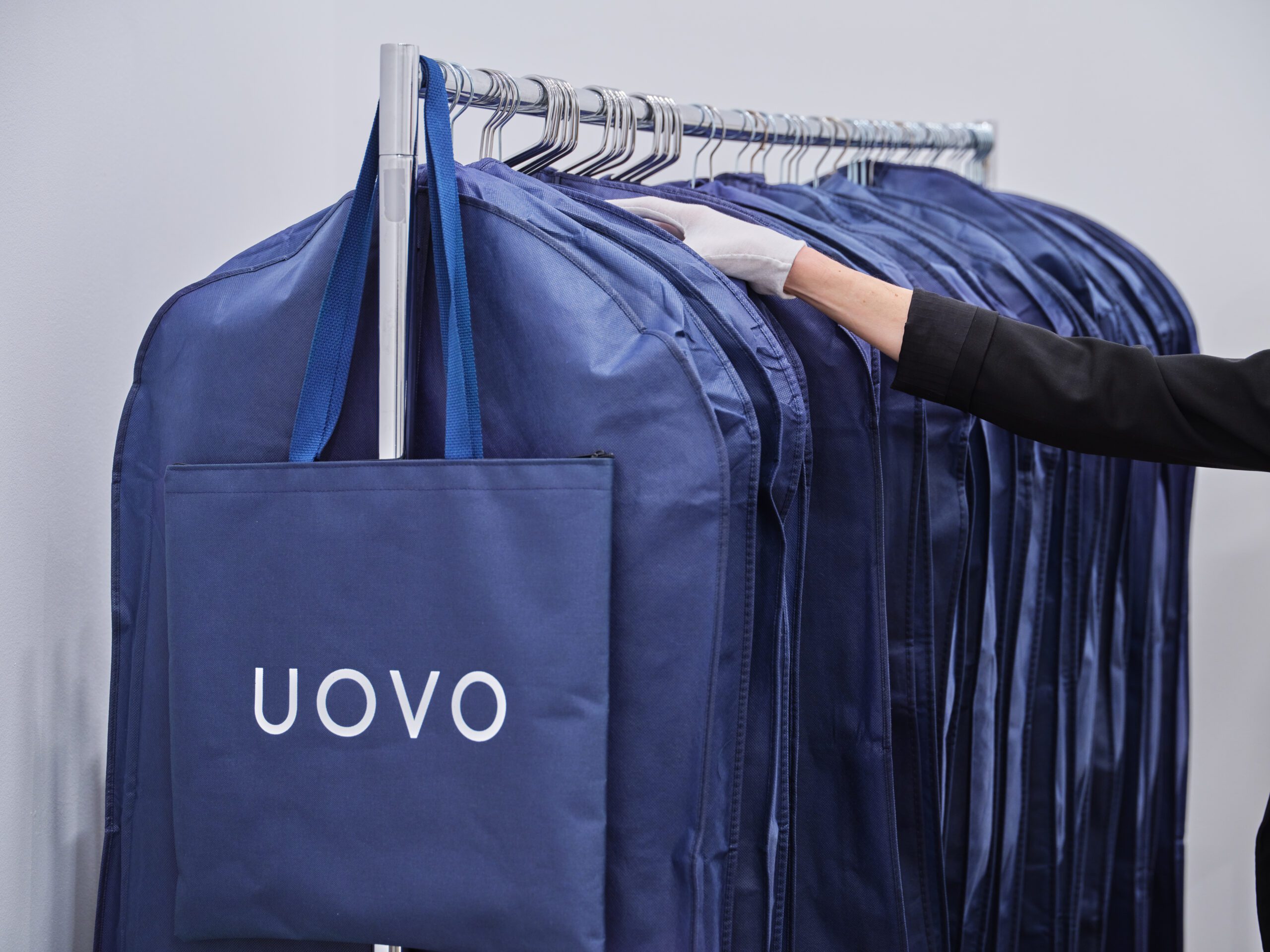 Fashion garment-storage bags hanging on a metal rack, carefully handled by UOVO wardrobe manager.